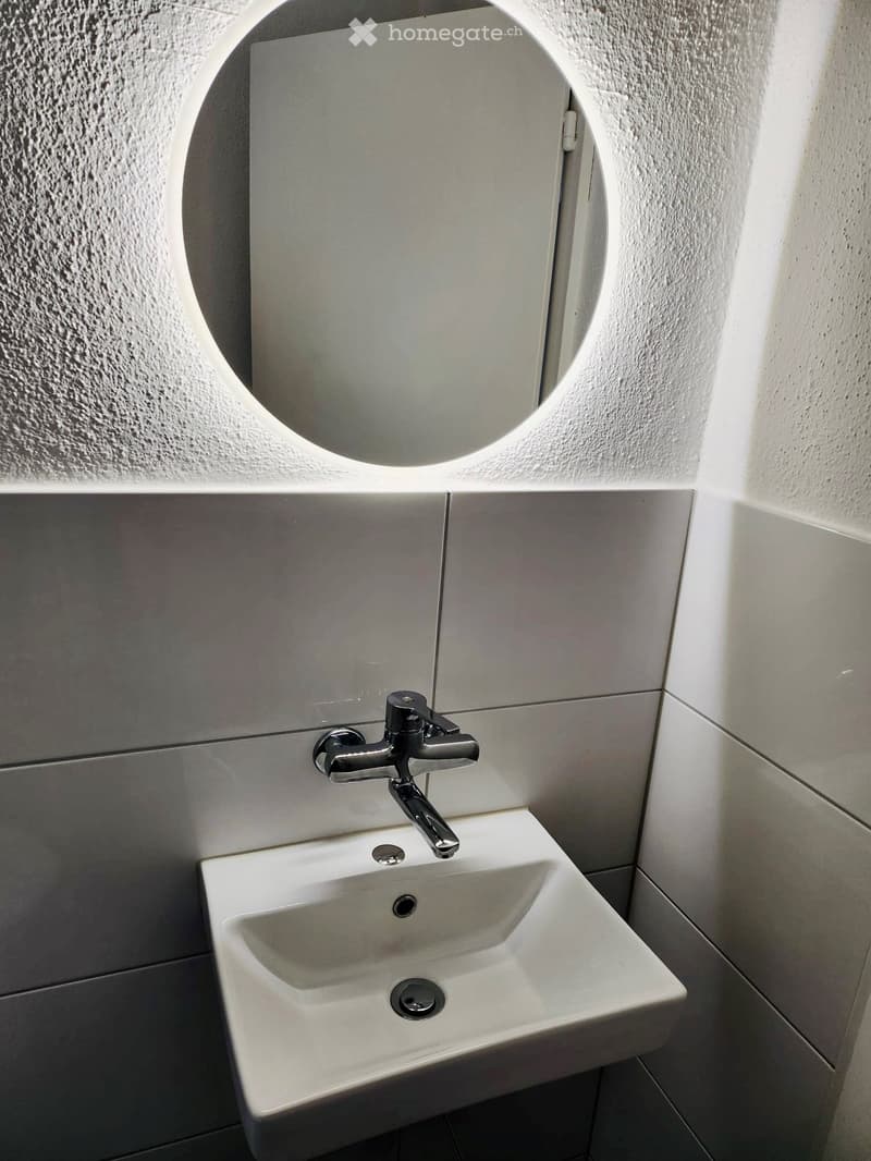 Modern bathroom with a white sink, chrome faucet, and a round mirror above it.