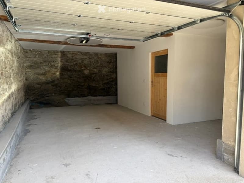 Empty garage with concrete floor, exposed wooden beams, and a single wooden door leading outside.