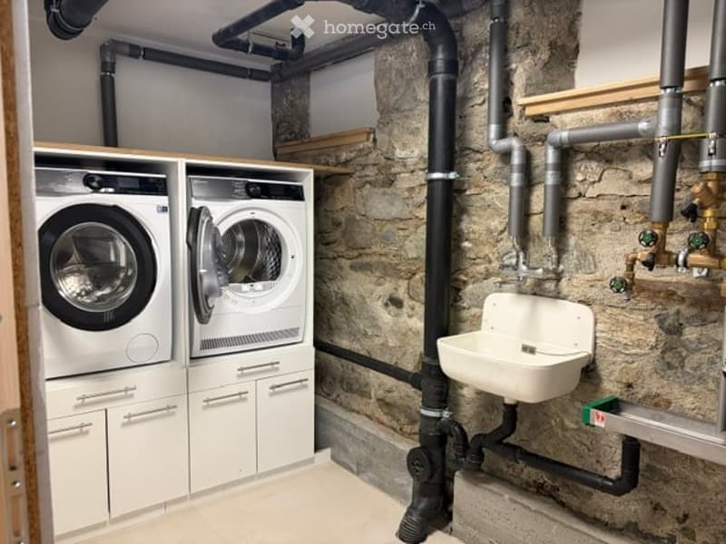 Modern basement bathroom with a white sink, a stacked washer and dryer unit, and exposed stone walls.