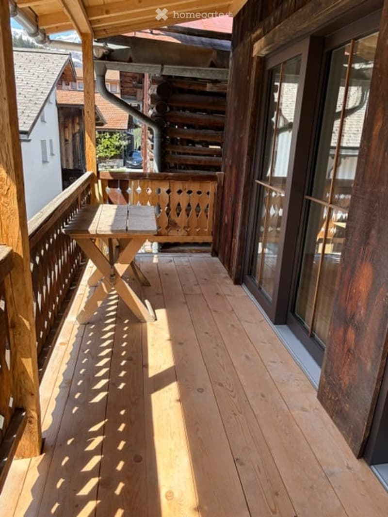 Wooden balcony with a small table, wooden railing, and glass doors leading to the interior.