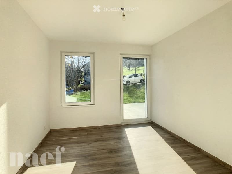 Empty room with wooden flooring, white walls, and large windows and sliding doors leading to an outdoor area.