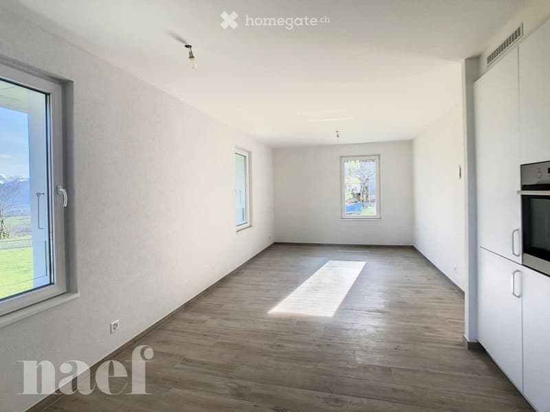 Empty room with wooden flooring, white walls, and large windows allowing natural light. No furniture or equipment is present.