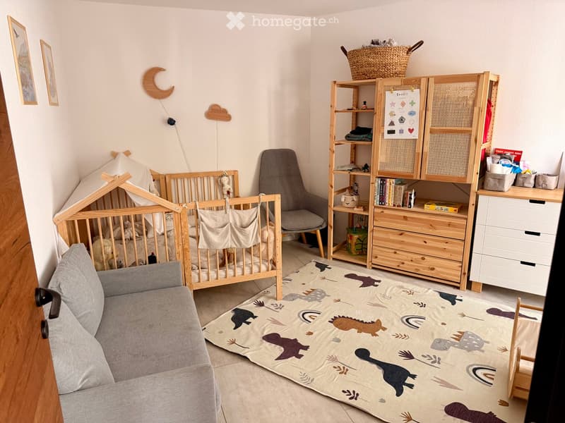 A well-organized children's bedroom with a crib, a sofa, a chair, a shelf, a storage unit, a wicker basket, and a rug with dinosaur patterns.
