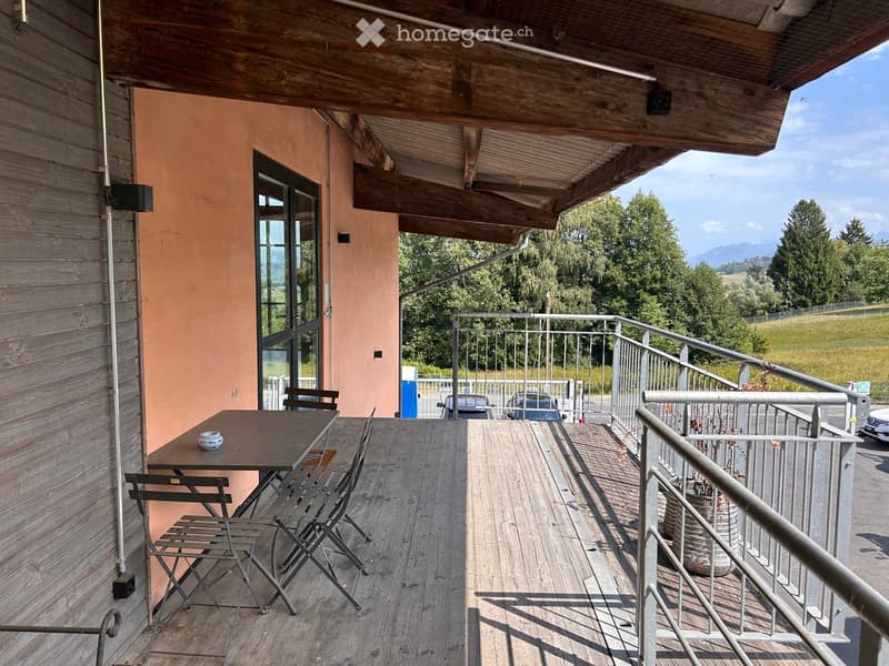 Balcony with wooden floor, metal railing, table, and chairs, overlooking a scenic view of trees and mountains.