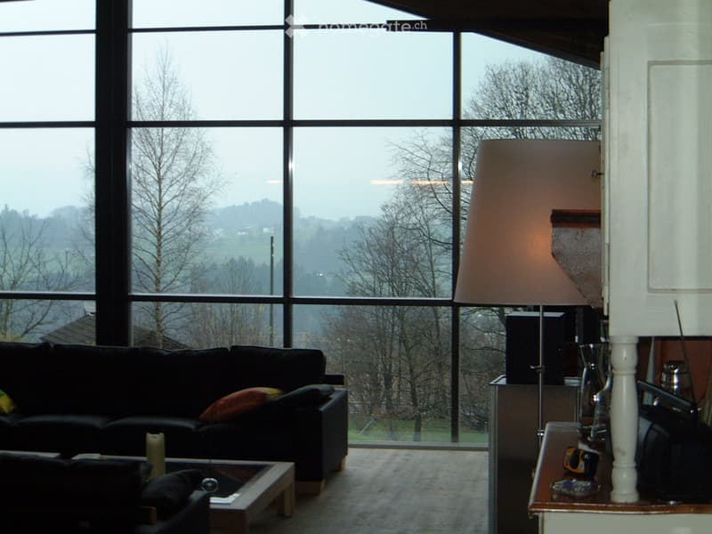 Modern living room with large windows offering a scenic view, featuring a black sofa, coffee table, and floor lamp.