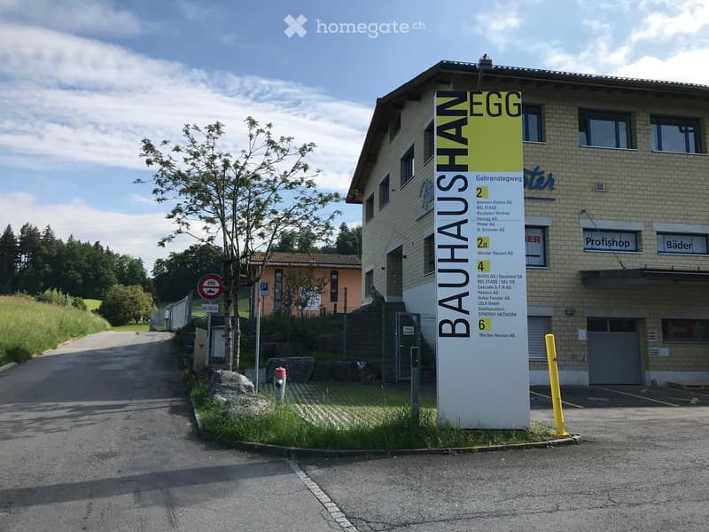 A multi-story building with a sign reading "BAUHAUS EGG" and a list of tenant companies, surrounded by a paved area and greenery.
