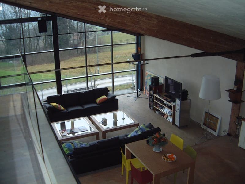 A modern living room with large windows, a black sofa, a coffee table, a dining table with chairs, and a TV stand with a screen.