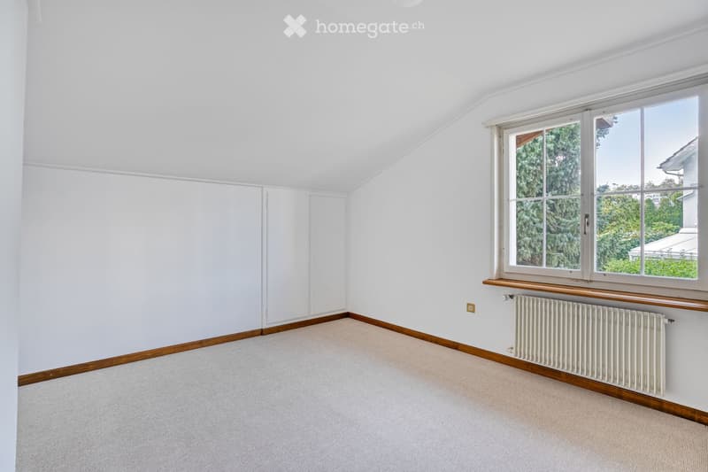 Empty room with white walls, wooden baseboards, carpeted floor, large window with wooden sill, radiator, and built-in closet.