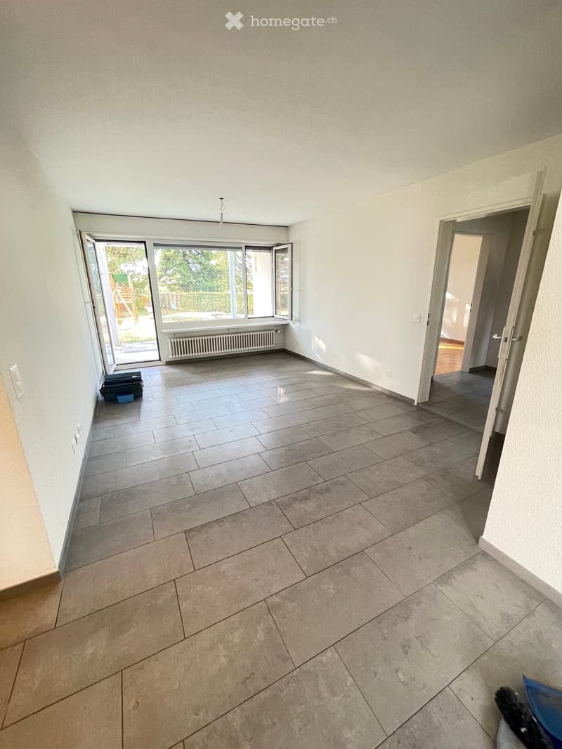 Empty room with tiled floor, white walls, large sliding glass door leading to outdoor area, radiator, and visible doorway to another room.