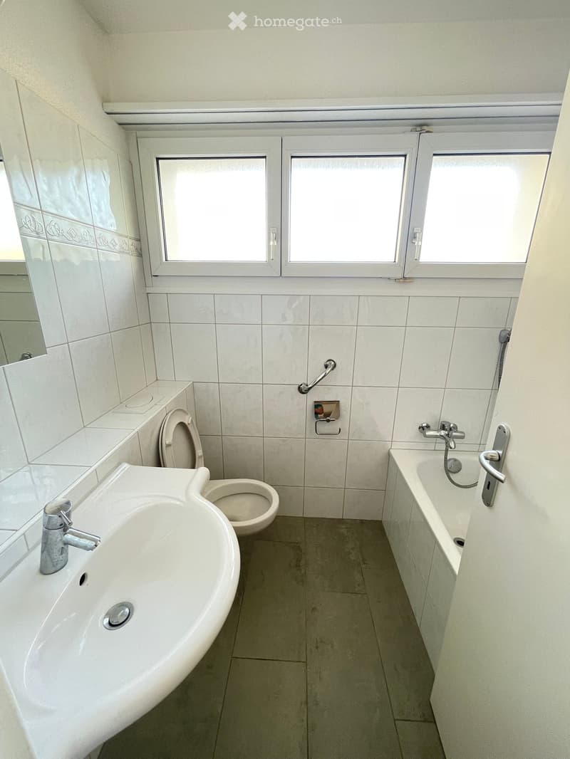 Bathroom with a sink, toilet, bathtub, and a mirror. The room has tiled walls and a window with multiple panes.