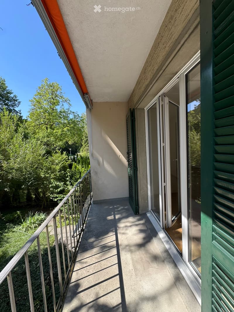 Balcony with metal railing, green shutters, and sliding glass doors leading to the interior.