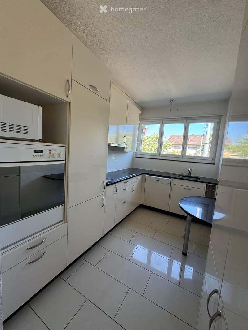 Modern kitchen with white cabinets, stainless steel appliances, tiled floor, and a small round table with a single chair.