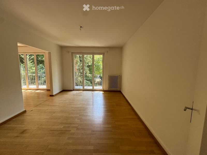 Empty room with wooden flooring, large windows, and sliding glass doors leading to a balcony.