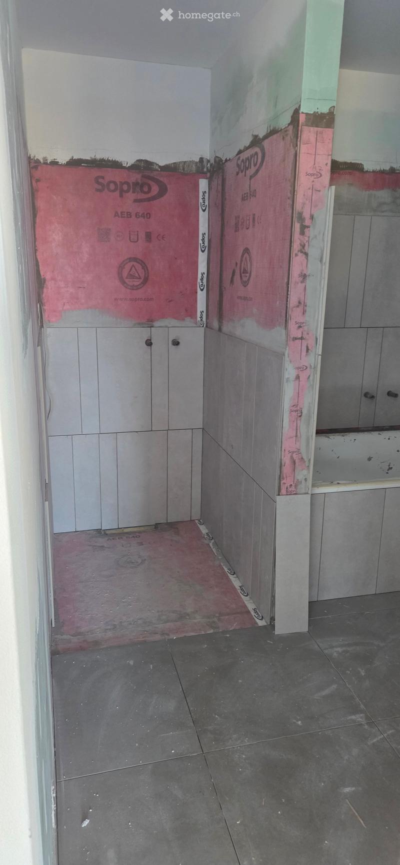 Empty room with unfinished walls and floor, showing insulation and construction materials.