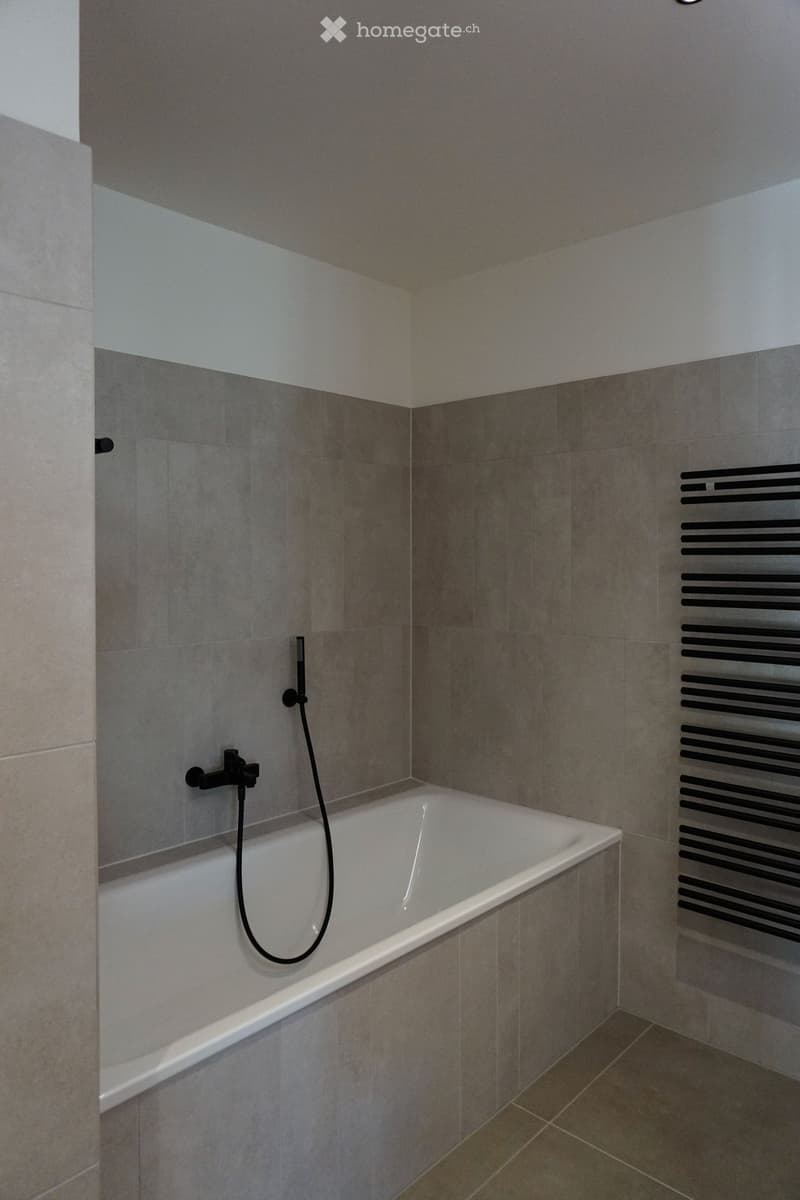 Modern bathroom with a white bathtub, black shower hose, and a radiator on the wall.