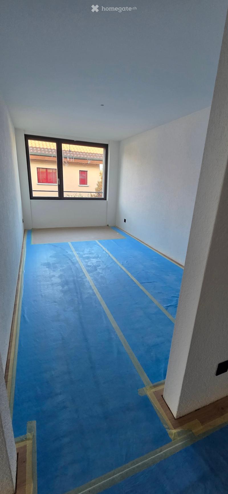 Empty room with light blue walls and a blue floor, featuring a large window with a view of a neighboring building.