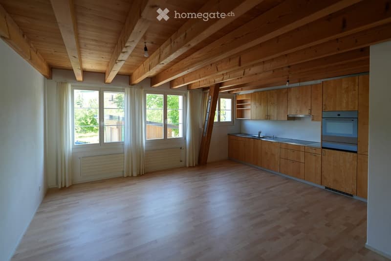 Bright kitchen with wooden cabinets, a sink, and an oven, featuring large windows and wooden flooring.
