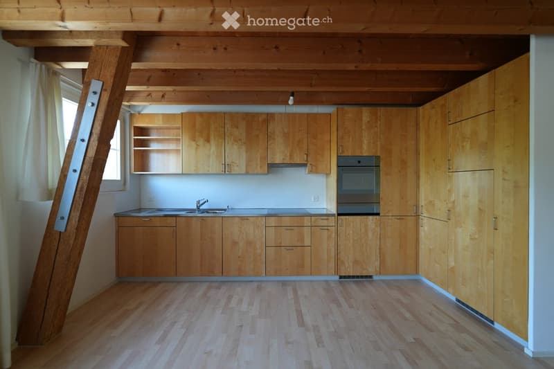Modern kitchen with light wooden cabinets, stainless steel sink, and built-in oven. Exposed wooden beams on the ceiling and wooden flooring.