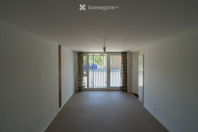 Empty room with beige walls, carpeted floor, and large double doors leading outside. No furniture or equipment present.