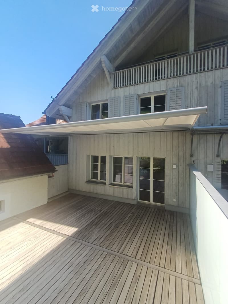 Wooden deck with a retractable awning, large windows, and a balcony railing.