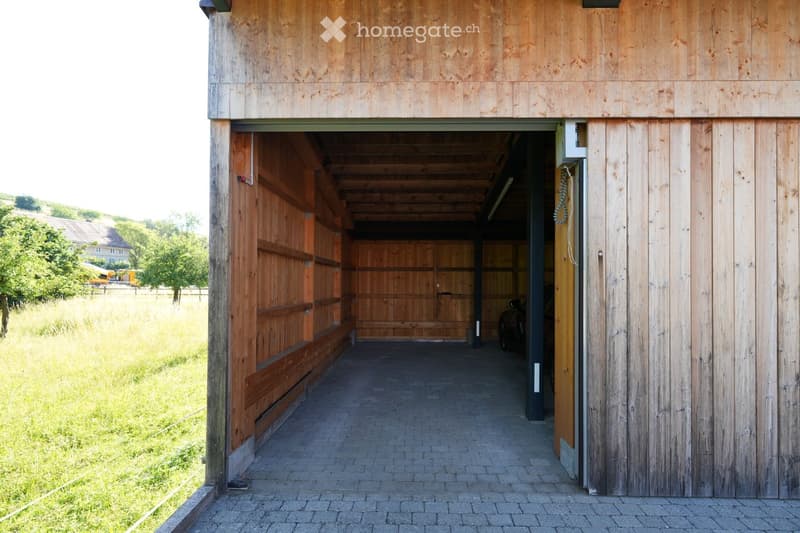 Wooden garage with large open doors, brick pathway leading inside, visible storage space and equipment inside.