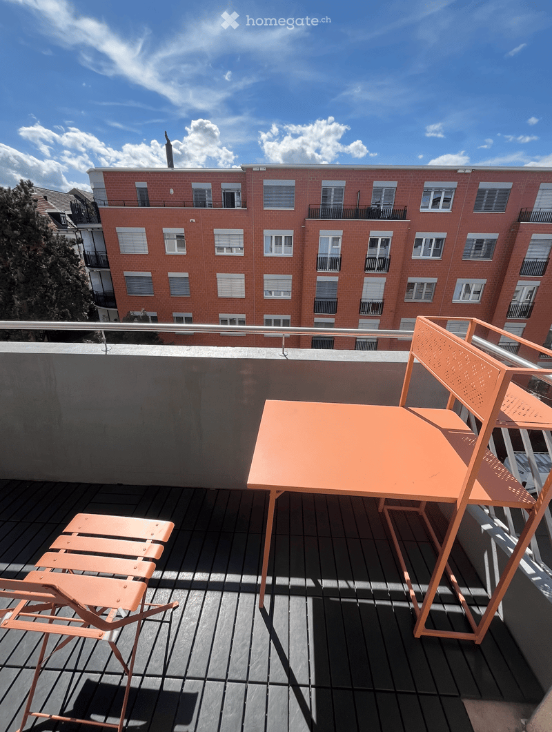 Balcony with orange table and chairs, overlooking a red brick apartment building.