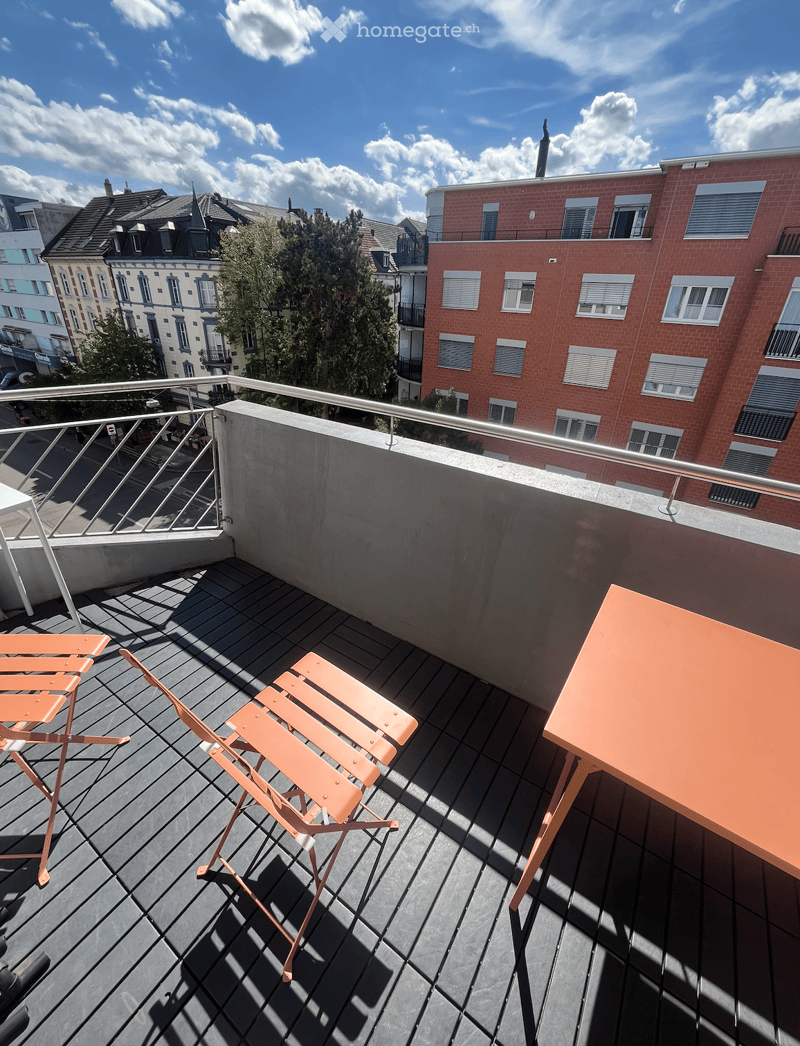 Balcony with wooden decking, metal railing, and orange furniture including a table and chairs.