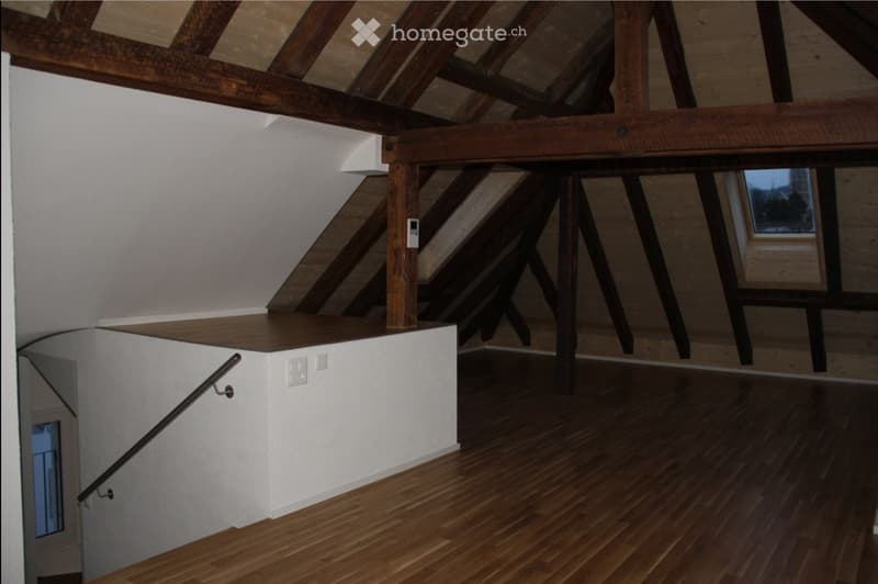 Staircase with wooden steps and handrail, white walls, exposed wooden beams, and a small landing area with built-in storage.