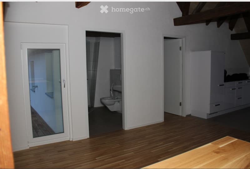 Empty room with wooden flooring, white walls, and three open doors leading to a bathroom, a closet, and another room.