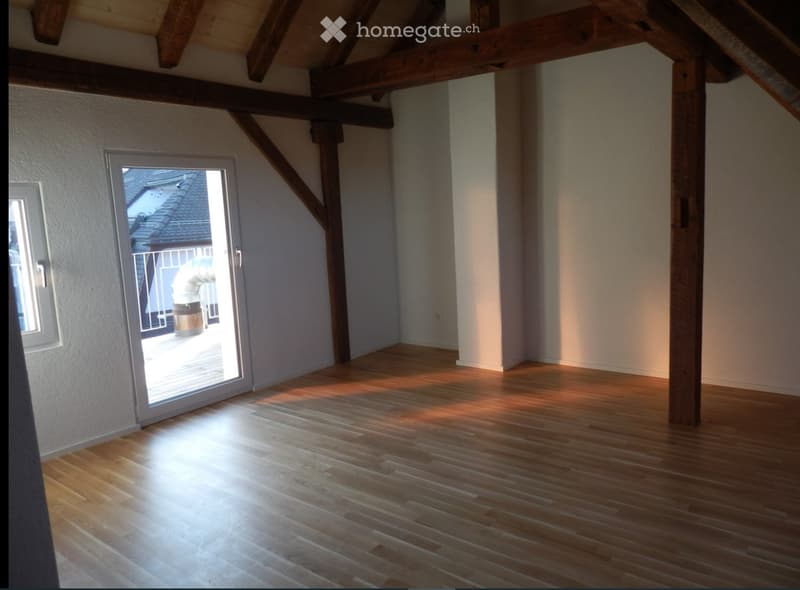 Empty room with wooden flooring, exposed wooden beams, and a sliding glass door leading to a balcony.