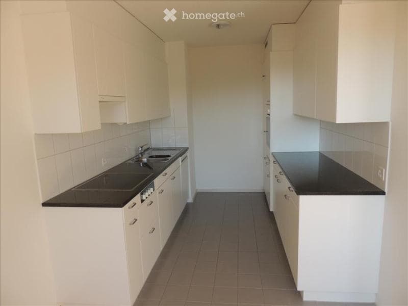 Modern kitchen with white cabinets, black countertops, and a sink. The space is clean and well-lit with tiled flooring.