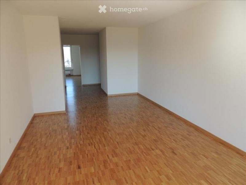 Empty room with wooden flooring and white walls, featuring a doorway leading to another room.