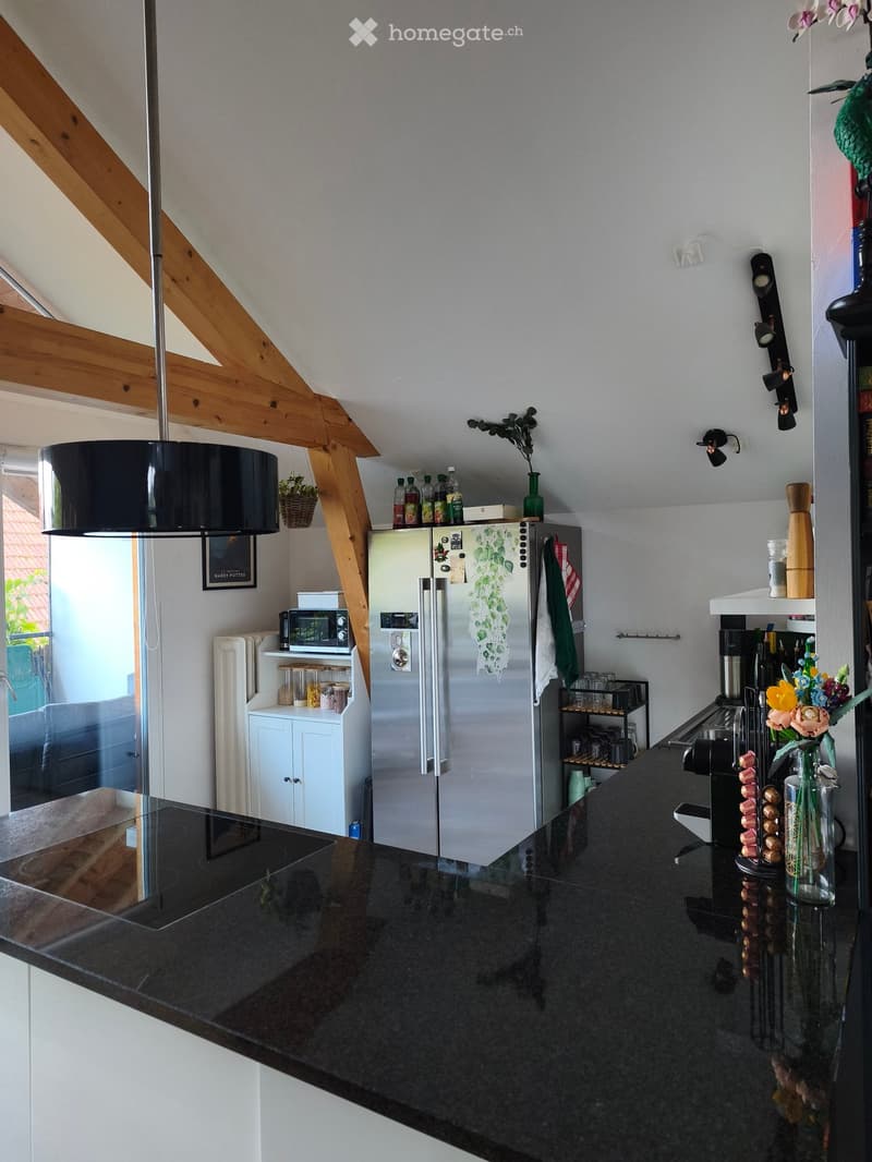 Modern kitchen with stainless steel appliances, black countertop, and wooden beams on the ceiling. Includes a refrigerator, microwave, oven, coffee maker, and various kitchen items.