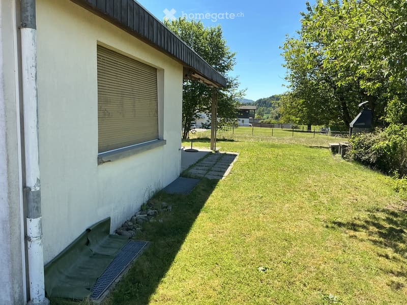 Lawn area adjacent to a house with a covered patio, a small shed, and a view of a rural landscape with trees and distant mountains.