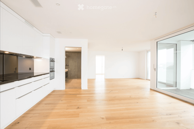 Bright, open-plan space with light wooden flooring, white cabinetry, and large glass doors leading to a balcony. The room is empty, with no furniture or appliances visible.