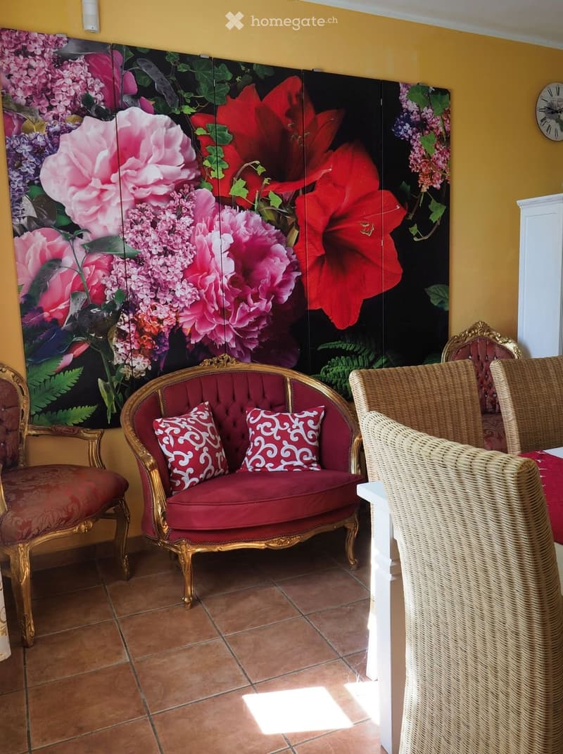 A cozy living room with a red upholstered sofa, two ornate chairs, and a large decorative screen with floral designs.