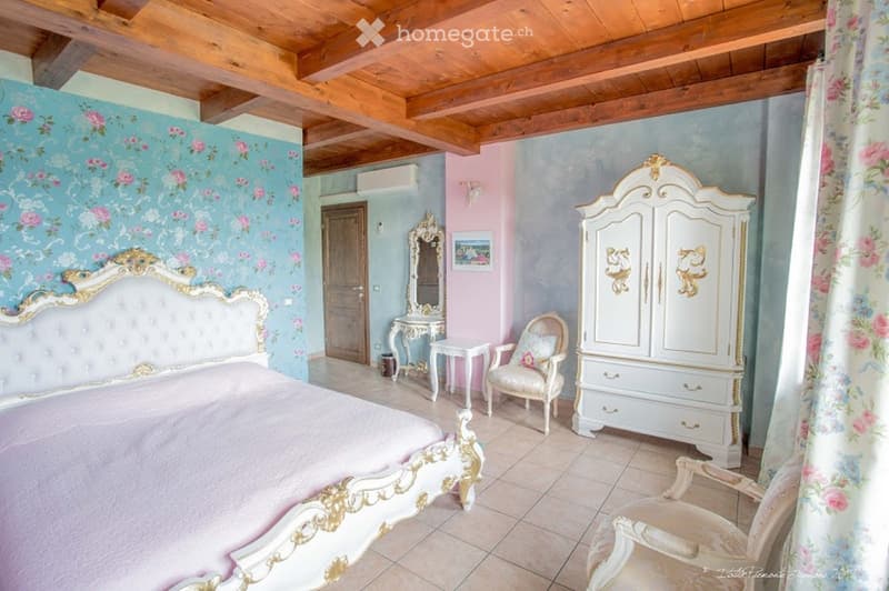Elegant bedroom with a tufted headboard, floral wallpaper, ornate furniture, and a wooden ceiling.