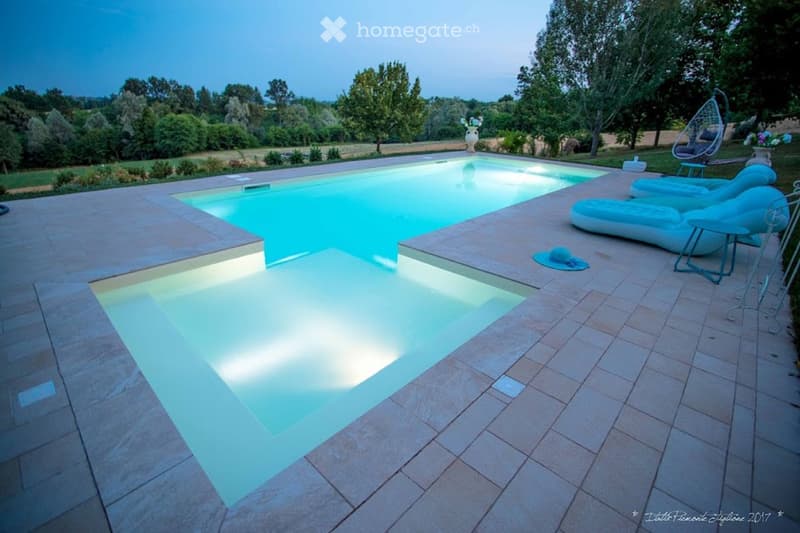 Outdoor area with a swimming pool, lounge chairs, and a scenic view of trees and fields.