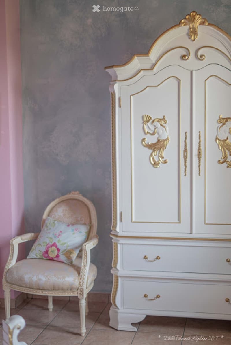 Elegant white and gold furniture set including a chair with floral pillow, an ornate armchair, and a tall cabinet with gold detailing.