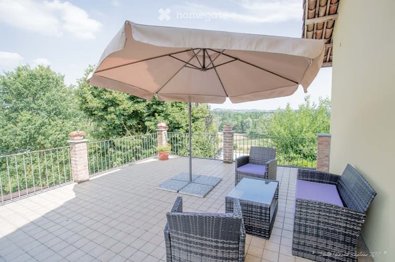 Balcony with tiled floor, metal railing, umbrella, glass table, and wicker chairs.