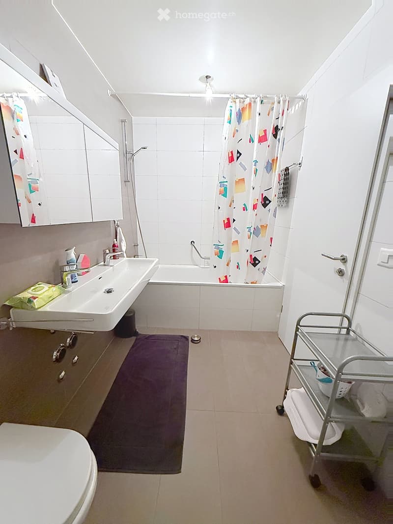 Bathroom with a sink, bathtub, shower curtain, mirror, towel rack, and a small cart with towels and items.