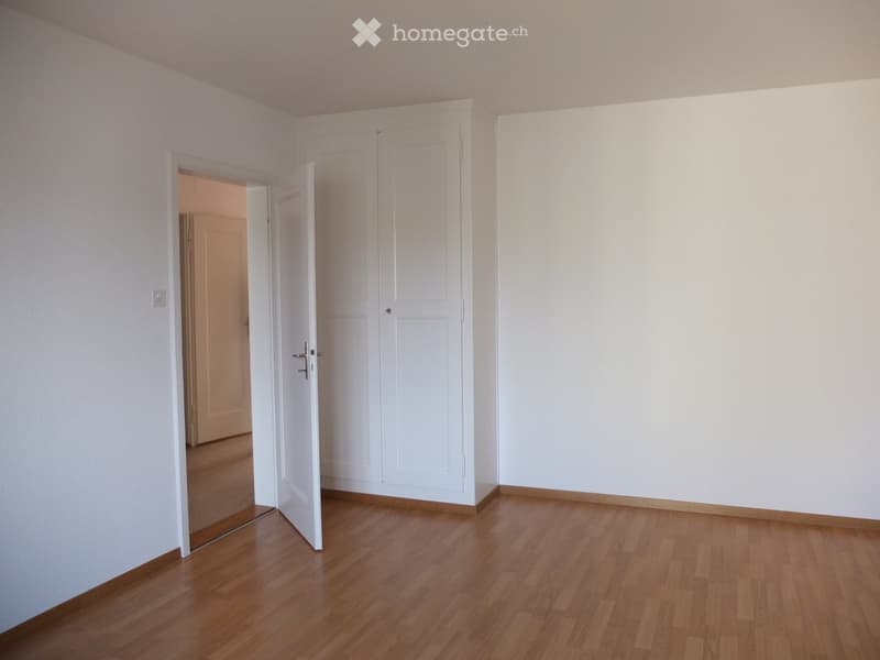 Empty room with wooden flooring, white walls, and a closed white door. No furniture or equipment visible.