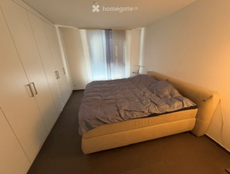 Modern bedroom with a large bed, dark bedding, and white built-in wardrobes. Large windows with blinds allow natural light to fill the space.