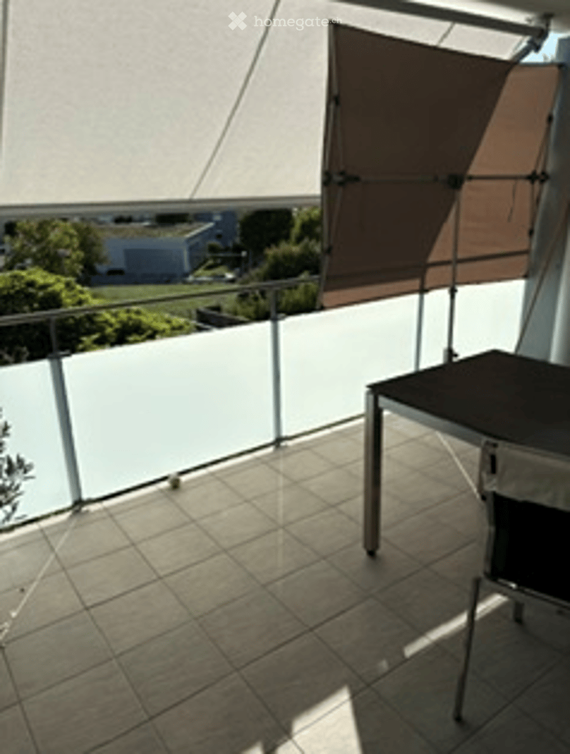 Balcony with tiled floor, glass railing, and a table with a chair.