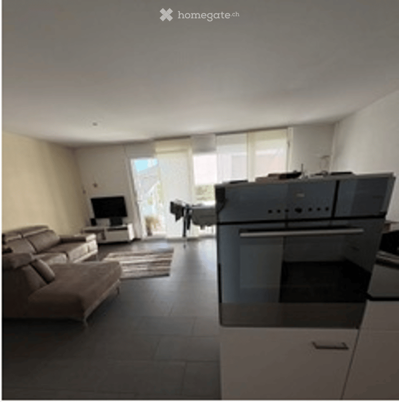Bright, open-plan living and dining area with a brown leather sofa, coffee table, flat-screen TV, and modern oven. Large sliding glass doors lead to a balcony.