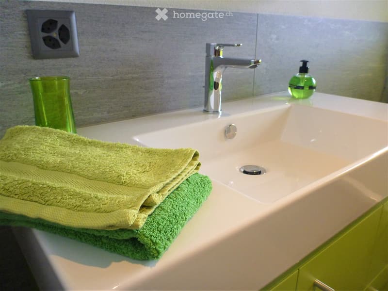 Bathroom. Bathroom sink with folded towels, soap, and a cup on the counter. Green accents.