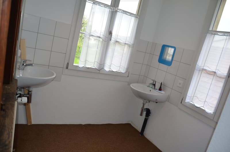 Bathroom with two sinks, tiled walls, and windows with white curtains.