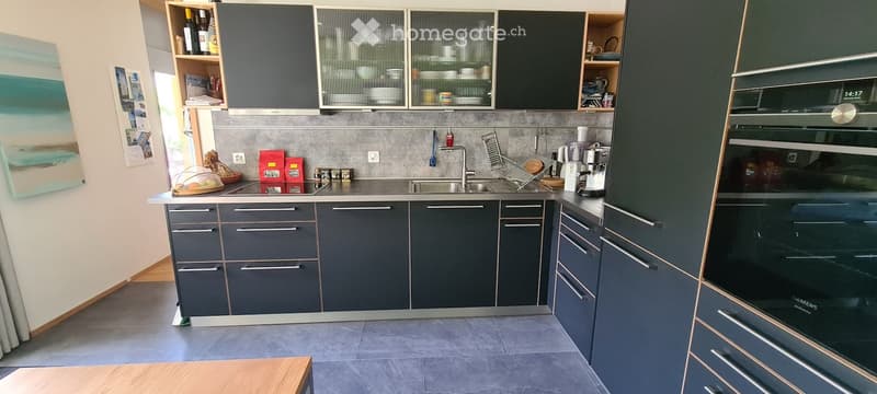 Modern kitchen with grey cabinets, stainless steel sink, coffee maker, and built-in oven.