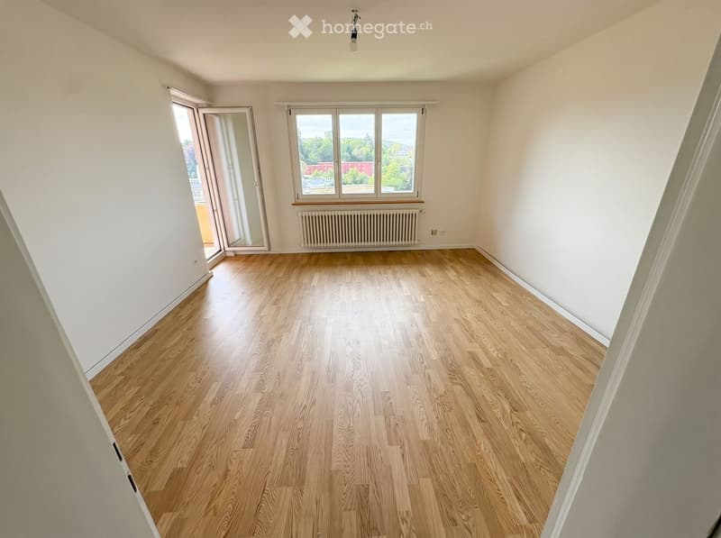 Empty room with wooden flooring, white walls, large windows, and a radiator. No furniture or equipment present.
