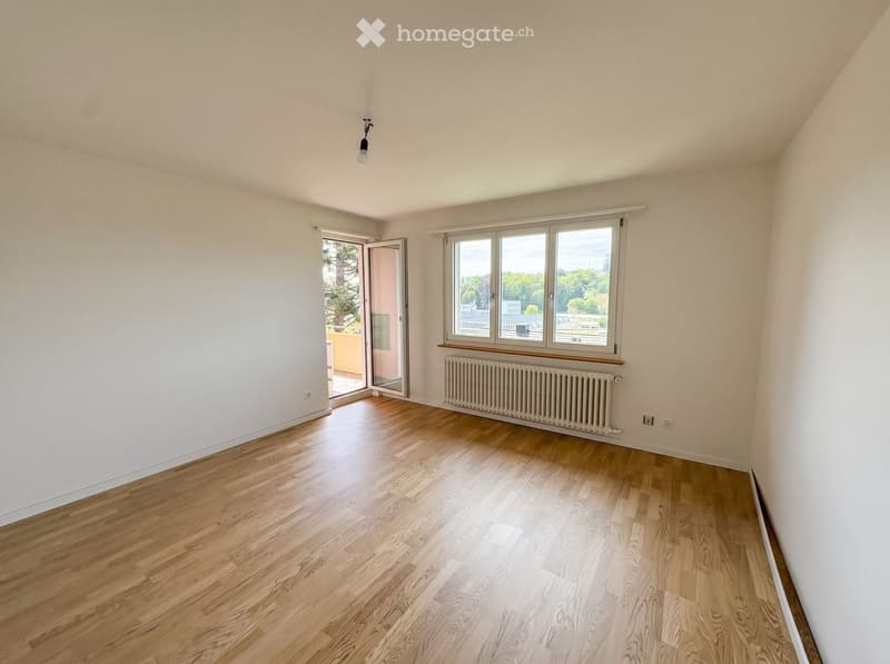 Empty room with wooden flooring, white walls, large windows, radiator, and a sliding glass door leading to a balcony.